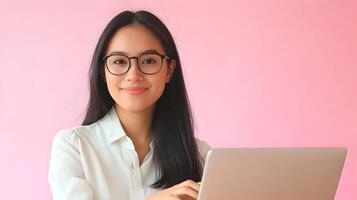 Confident and Capable Asian Female Professional Wearing Eyeglasses Sitting at Desk Using Laptop Computer in Modern Office Environment,Representing IT Specialist,Software Engineer or Developer photo