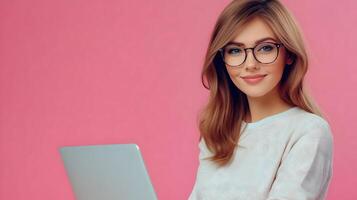 Portrait of a confident and successful young woman wearing glasses and using a laptop computer in a pink studio setting. She appears to be an information technology specialist,software engineer. photo