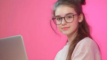 Confident Young Female Tech Professional Wearing Eyeglasses and Smiling While Using Laptop Computer in Studio with Pink Background photo