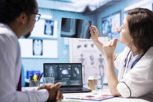 Woman physician reading x ray diagnostics for a patient in medical office, doing a test results scan interpretation to help person with disease. Providing treatment and advice for recovery. photo