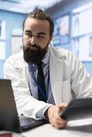General practitioner working with healthcare records and test results to find the diagnosis in his office, examining x rays and reports. Doctor doing research for disease prevention and treatment. photo