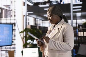 Businesswoman using tablet to analyze market trends and data in office. Entrepreneur developing trading strategies and algorithms, checking paperwork on electronic device photo