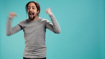 Man jumping from joy in excitement while cheering for favorite sports team, studio background. Person celebrating after victory, showing intense enthusiasm, supporting team during game, camera B photo