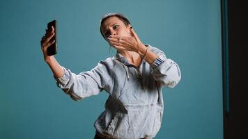 Silly confident woman recording a while she shows groovy dance moves, filming on her smartphone and fooling around in studio. Funky bold edgy person being funny. Camera A. photo