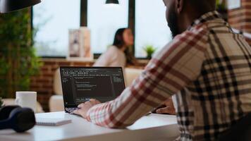 African american software engineer works on a laptop typing code for a development project. Technical specialist multitasking, debugging and using advanced digital tools for coding. Camera B. photo