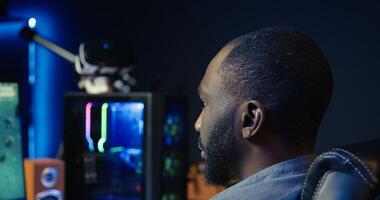 Man at home plays online multiplayer spaceship videogame with friends, relaxing, close up. African american player, flying spacecraft, enjoying leisure time in RGB lights adorn apartment, camera B photo