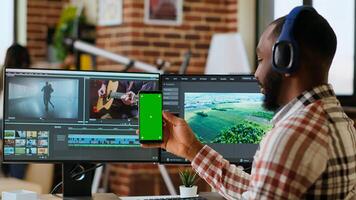 Male editor works on a movie project in a creative software next to chroma key, multitasking between timeline editing and color grading using dual monitors and tech tools. Camera B. photo