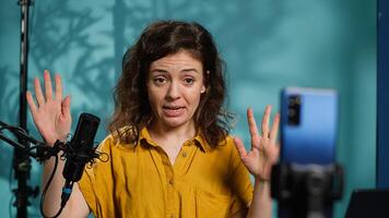 Mobile phone used for recording cheerful woman chatting with online audience, filming in home studio. Media star discussing with fans during live broadcast stream filmed with cellphone, camera A photo