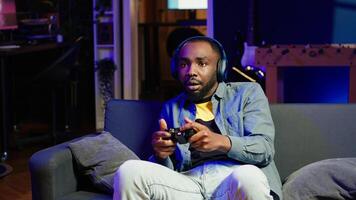 Enthusiastic gamer on couch using controller and headphones to play videogame in neon lit apartment. Player in RGB illuminated living room using high tech gaming console joystick, camera A photo