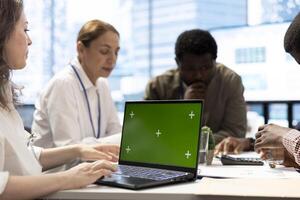 Diverse enterprise staff using a laptop with copy space display during a briefing meeting, establishing the future of the multinational company. Employees and managers in a conference. photo