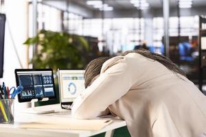 Tired businesswoman at work sleeping on desk while working on laptop to solve business tasks, suffering burnout. Sleepy employee dozing off in office after working overtime to finish project photo