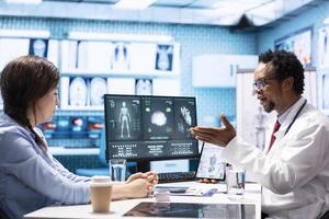 General practitioner giving the right diagnosis to woman patient, attending a checkup consultation in medical cabinet. Doctor explaining x ray imaging and scan results, care management. photo
