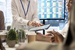 Diverse group of professionals meeting to discuss a new development strategy, utilizing infographics and monthly analysis numbers to reach target and accomplish organizational goals. Close up. photo