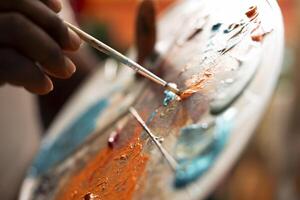 In an art studio, painter mixes multiple watercolor paints on a palette to create a new artwork on canvas. Skilled man painting with tools and showing his imagination, artistic creation. Close up. photo