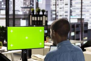 Male business manager at desk looking at mockup screen and solving tasks for company objectives accomplishment. Fighting for performance goals to ensure successful corporate outcomes. photo