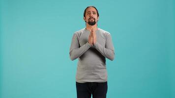 Portrait of man putting hands together in begging gesture, making wish, hoping for good news isolated over studio background. Person waiting for results, praying for positive outcome, camera A photo