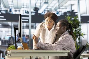 Young employee and manager gathered around a computer discussing objectives and strategizing solutions to solve administrative tasks faster. Aligning business goals and milestones. photo