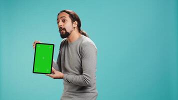Happy man holding green screen tablet, doing recommendation. Cheerful person presenting mockup device, showing positive feedback, isolated over studio background, camera B photo