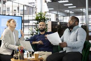Upset diverse team of employees arguing after making mistake while writing revenue figures on documents in office. Mad staff members fighting during dispute over company statistical numbers photo