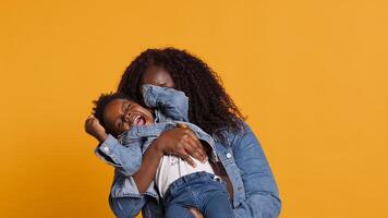 Smiling african american mom carrying her sweet little boy in studio, embracing him and bonding in front of the camera. Cheerful mother and cute small baby posing together, loving mommy. Camera A. photo