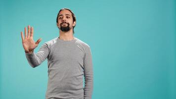 Assertive man doing stop hand gesture sign, studio backdrop. Annoyed person doing firm halt sign gesturing, wishing to end concept, isolated over blue studio background, camera B photo