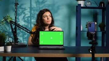 Influencer in home studio using recording tech to capture live broadcast, reviewing chroma key laptop. Online show host filming electronics haul, presenting green screen notebook for viewers, camera B photo