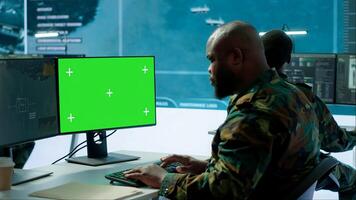Military specialist monitors satellite data next to green screen display, working at command post with high tech gear to support army defense operations. Coordinates strategic missions. Camera A. photo