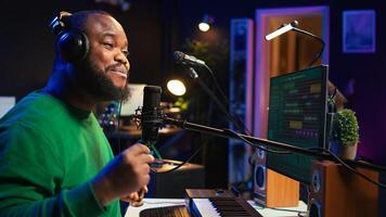 Confident artist singer performing a song on microphone in home studio, recording his audio files and manipulating raw sound on professional editing software. Music production. Camera B. photo