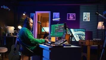Audio engineer working in home studio with digital software on pc, playing piano keys and editing audio recordings. Musician producer creating tracks on midi controller keyboard notes. Camera B. photo