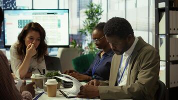 Shareholder examining infographics and resource allocation on tablet, gathering with associates for a strategy session. Utilizing data analytics to develop innovative solutions for growth. Camera B. photo