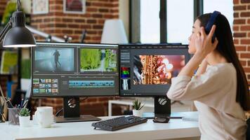 Asian filmmaker woman putting headphones on and working on production at a home office, mixing clips. Office setup with a software perfect for color grading in post production. Camera B. photo