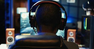African american player in neon illuminated apartment paying close attention to computer screen during videogame competitive match. Person competing in internet esports tournament, camera B photo