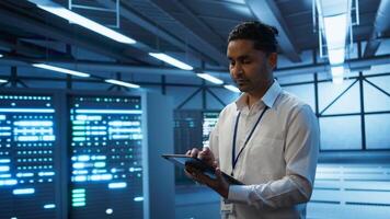 Engineer walking in data center, monitoring security threats, implementing cybersecurity measures. Indian man ensuring compliance with regulations to protect data center gear, camera B photo