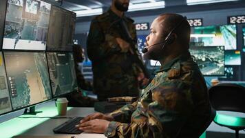 Military dispatcher relays info from army intelligence analysts to troops on front lines, close up shot. Radio communications operator wearing uniform talking in headset mic, camera B photo