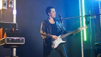 Confident musician performing live in a spotlight illuminated studio, surrounded by audio equipment and lights. Rocker doing a live performance in a rebellious style, bold attitude. Camera A. photo