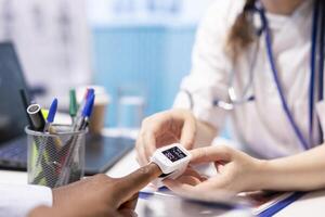 Medical specialist takes the oxygen saturation measurement and checking vital signs during a routine check up with her patient. Medic using an oximeter for accurate readings in office. Close up. photo