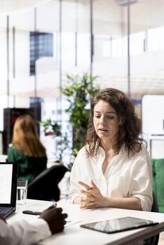 Human resources manager asking interview questions to vet selected applicants and ensure their skills match role needs. Headhunters in startup workspace assessing candidate work experience photo