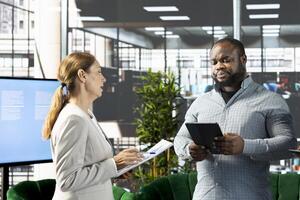 Teamworking businesspeople in startup company looking at financial business documents on tablet. Coworkers in office checking accounting figures on device, talking about data, doing comparison photo