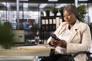 Businesswoman looking over business revenue charts and diagrams on mobile phone in office. Entrepreneur analyzing financial statistics on laptop and smartphone, trying to find strategic insights photo