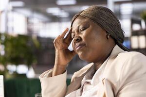 Stressed worker feeling troubling headache while working to solve business tasks, suffering burnout. Close up of staff member in office having migraine after working overtime photo