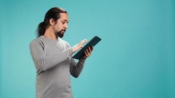 Man browsing though financial audit report on tablet, isolated over blue studio background. Worker reading paperwork on digital portable device, solving business tasks, camera B photo