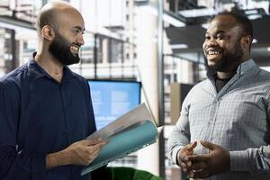Upbeat startup CEO attends meeting to talk about new business vision with executive board member, presenting him documents. Joyous employee holding files, pitching investment strategy to manager photo