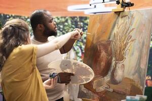 Team of artists painting a beautiful rustic creation on canvas, mixing colors together on a palette to create a nature inspired design. Diverse painters enjoy quality time in art studio. photo