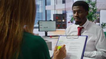 HR staff and applicant discussing the employment contract terms during the interview, providing explanations and clarifications. Job candidate reading the work agreement in high end office. Camera B. photo