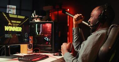 Man feeling happy while playing videogames on computer desktop with headphones on, celebrating victory. Cheerful gamer smiling after winning game on gaming PC while at home, camera B photo