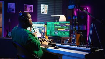 Confident music composer mixing sounds on digital audio software, creating a cool atmosphere in his home studio. Young cheerful producer composing new soundtracks with stereo gear. Camera B. photo