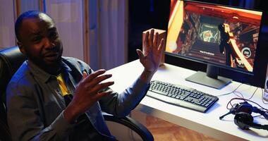 African american man teaching subscribers professional esports skills and how to play game. Media star on gaming chair chatting with viewers, filming gaming tutorial, camera B photo
