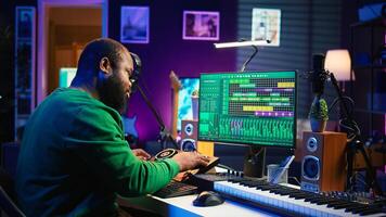 Skilled male composer producing new songs on his mixing console, operating on professional gear in home studio. Artist audio engineer twisting knobs to adjust sound levels on tracks. Camera B. photo