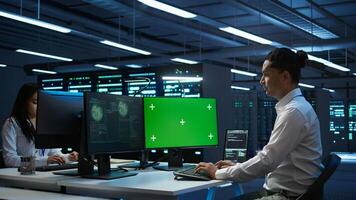 Engineer in server hub using green screen PC to stop hacker passing company firewall and stealing sensitive user data. Worker looking at mockup computer, seeing security breach notification, camera B photo