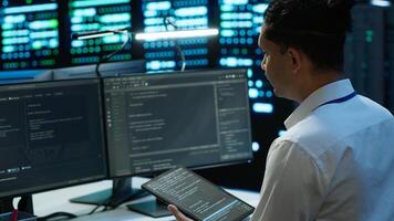 System administrator in data center installing software on computer, troubleshooting issues using tablet. IT staff member in server hub establishing performance benchmarks, camera A photo